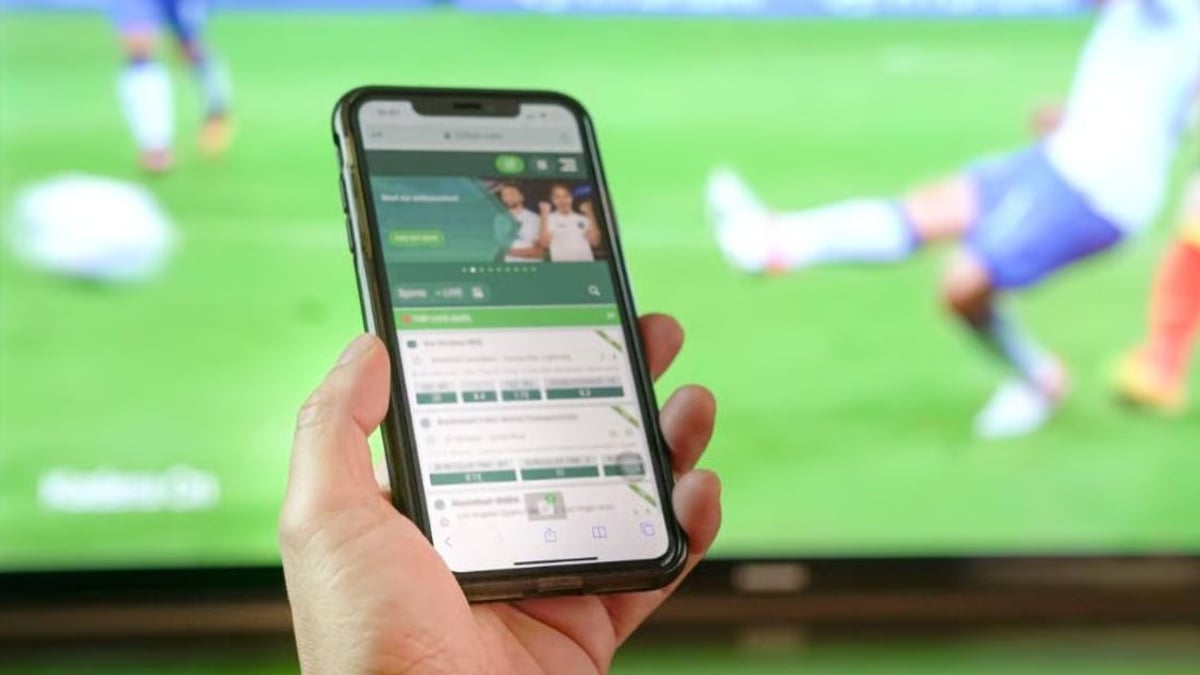 Point Spread vs. Spread Betting Explained: What They Mean and How They Differ Hand holding a mobile phone displaying a sports betting app